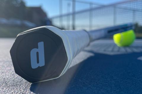 Tennis racket on tennis court next to a tennis ball