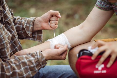 Person wrapping bandage around arm in woods.