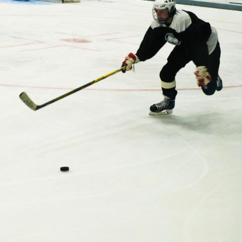 Hockey player reaching toward puck with hockey stick on ice.
